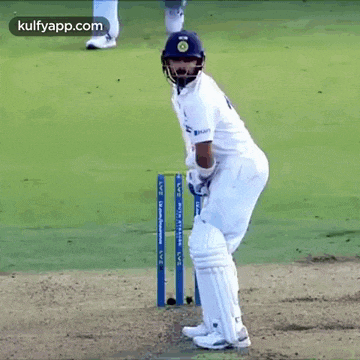 a cricket player is standing on the field holding a bat and a helmet .