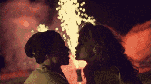 a man and woman kissing in front of a fireworks display