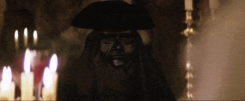 a statue of a man wearing a black mask and a hat is in front of candles .