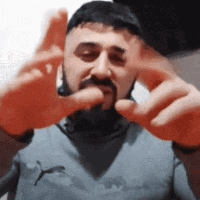 a man with a beard is making a funny face with his hands while wearing a puma shirt .