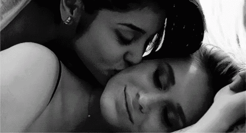 a woman is kissing another woman on the forehead while laying in bed .