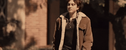 a man wearing a brown jacket with a fur collar stands in front of a brick building