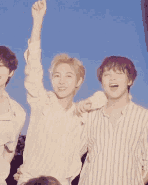 three young men are standing next to each other with one of them raising his fist in the air .