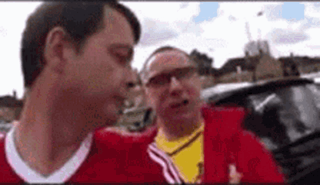 two men are standing next to each other in a parking lot .