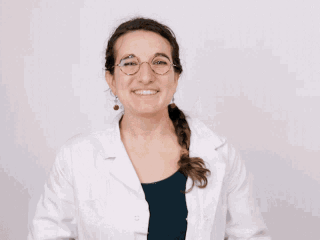 a woman wearing glasses and a white lab coat is making a funny face