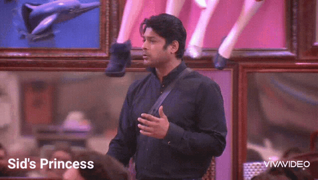 a man in a black shirt is standing in front of a wall with paintings and the words sid 's princess written below him