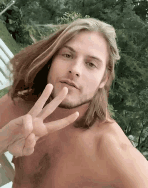 a shirtless man with long hair and a beard giving a peace sign