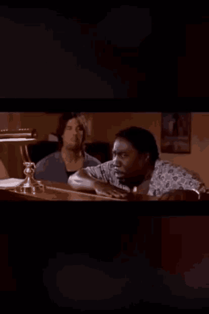 two men are sitting at a table in a dark room and one of them is smoking a cigarette