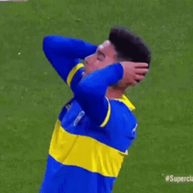 a man in a blue and yellow jersey is covering his ears with his hands