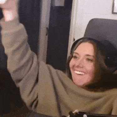 a woman wearing headphones and a sweater is sitting in a chair with her arms in the air .