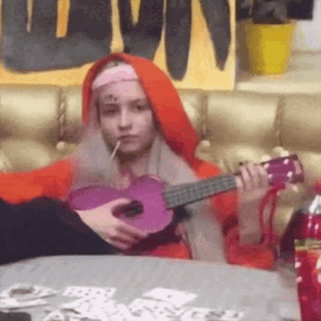a woman in a red riding hood costume is playing a purple ukulele while smoking a cigarette .