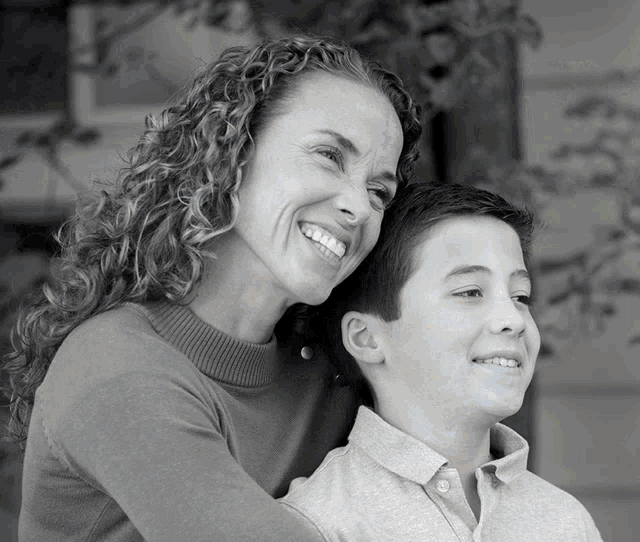 a woman with curly hair smiles while holding a boy