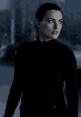 a woman in a black dress is standing in a dark room with her eyes closed .