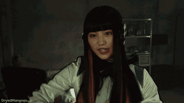 a girl with red hair is making a face with her hands and the website dryedmangoez.com is behind her