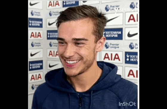 a man in a blue hoodie is smiling in front of a wall of aia logos