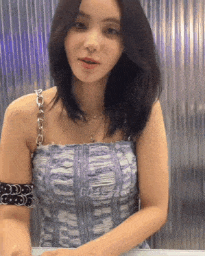 a woman wearing a denim top and a bracelet on her arm is standing in front of a wall .