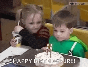 a boy and a girl are sitting at a table in front of a birthday cake .