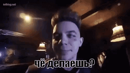 a man with a tattoo on his face is smiling in a dark room with a foreign language written on it .