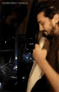 a man with a beard is standing in a dark room holding a piece of paper in his hand .