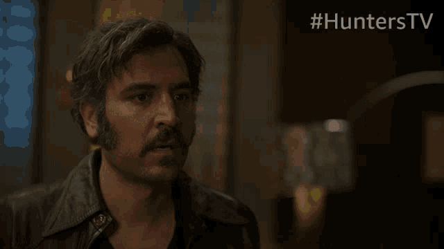 a man with a mustache is standing in front of a sign that says #hunters tv