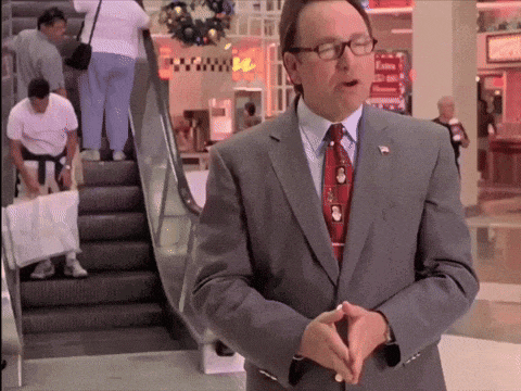 a man in a suit and tie stands in front of an escalator in a shopping mall