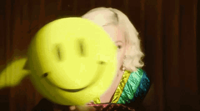 a woman is holding a yellow smiley face behind her face .