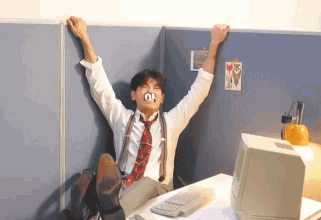 a man wearing a tie and suspenders is sitting at a desk with his feet up and his arms in the air