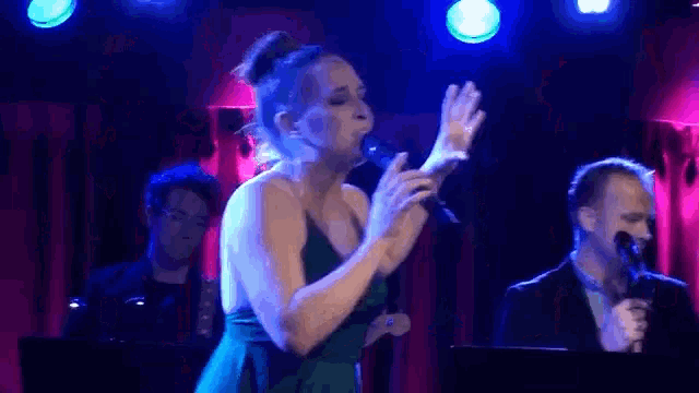 a woman is singing into a microphone on a stage in front of a man playing a keyboard .