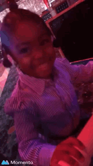 a little girl in a purple shirt is smiling and playing with a red light