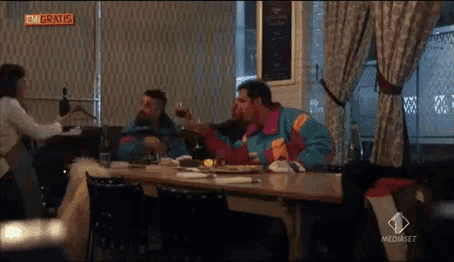 a man in a blue jacket is sitting at a table in a restaurant with a mediaset logo on the bottom right