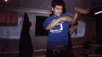a man wearing a blue shirt with the word grandpa on it is standing in a dark room .