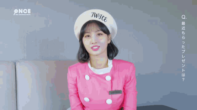 a woman in a pink dress and hat is standing in front of a pink building .