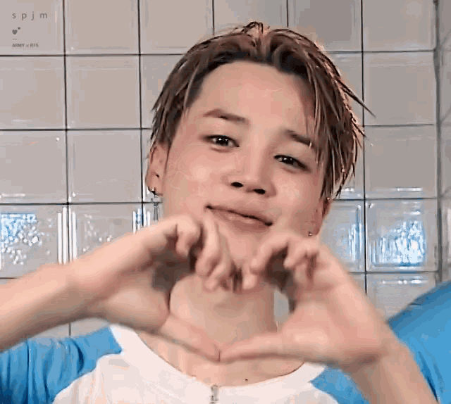 a young man is making a heart shape with his hands in front of a sign that says spjm