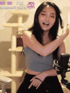 a woman in a crop top stands in front of a microphone and a cat tree