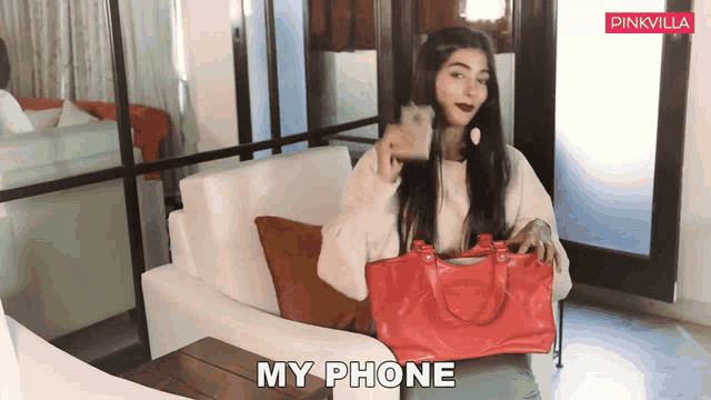 a woman sitting on a couch holding a red purse that says my phone on it