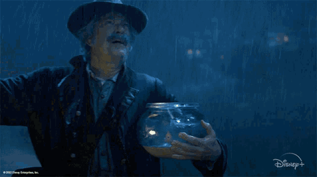 a man in a cowboy hat is holding a fish bowl with a disney logo on the bottom right