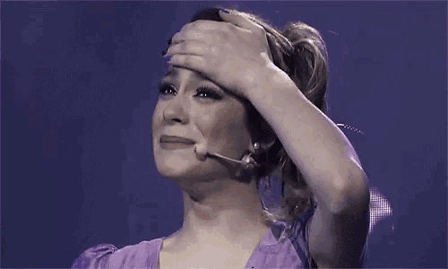 a woman in a purple dress is covering her face with her hand while wearing a microphone .