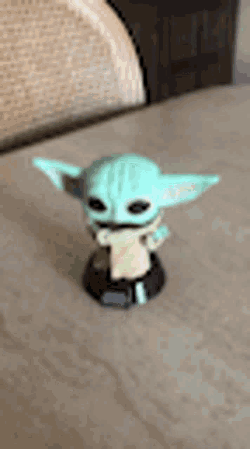 a green baby yoda figurine is sitting on a table .
