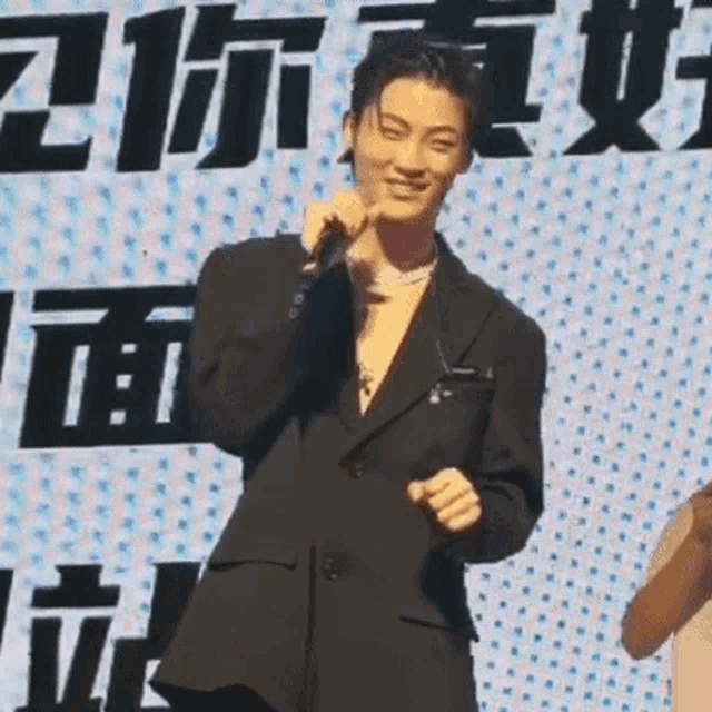 a man in a suit is holding a microphone and smiling while standing in front of a sign with chinese characters .