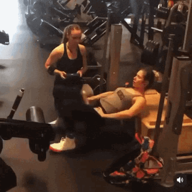 a woman is sitting on a machine in a gym while another woman watches .