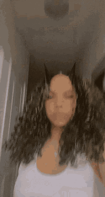 a woman with curly hair and horns on her head is wearing a white tank top and necklace .