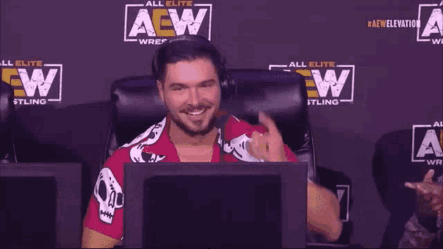 a man sitting in front of a monitor with a aew wrestling logo behind him