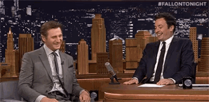 two men in suits and ties are sitting at a table with microphones talking to each other .