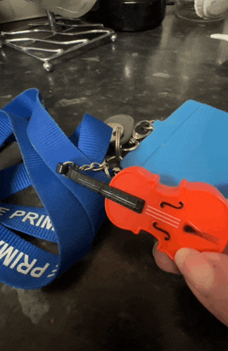 a person is holding a violin keychain next to a blue lanyard that says prime