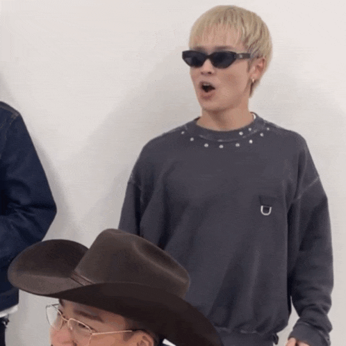 a man wearing sunglasses and a cowboy hat stands next to another man wearing glasses