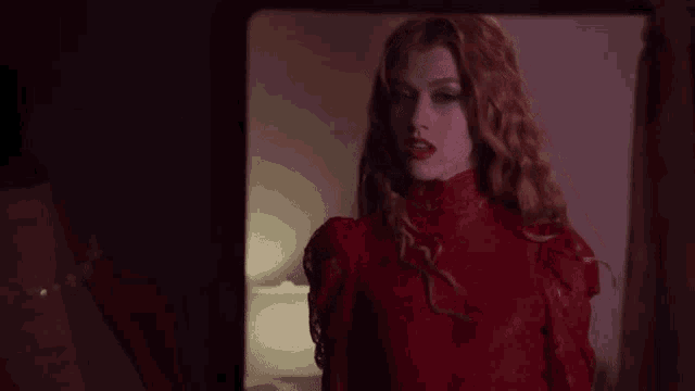 a woman in a red dress with red eyes is standing in front of a mirror .