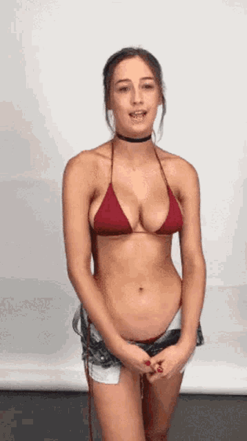 a woman in a red bikini top and shorts is standing in front of a white wall .
