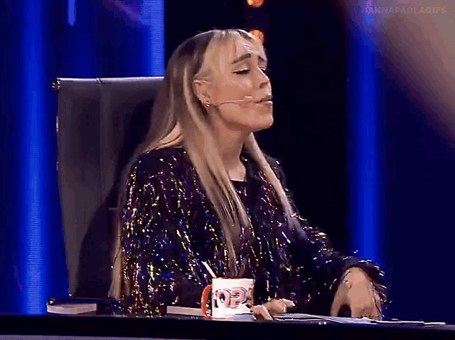 a woman in a sequined jacket sits at a desk with a cup that says ' i love you ' on it