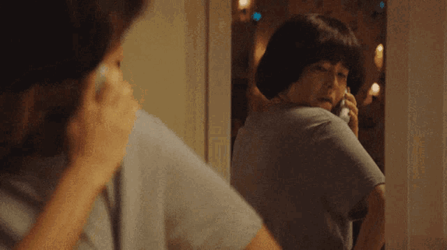 a woman talking on a phone while looking at herself in a mirror