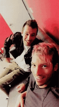 two men are sitting next to each other on a couch and smiling .